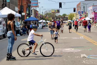 Diverse people of all ages walking and biking at Minneapolis Open Streets event with temporary festival booths along the sides of the street