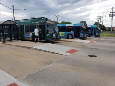 Three green and teal buses at a multi-lane bus station.