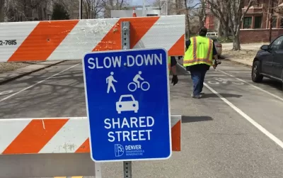 Close-up of blue "Slow Down - Shared Street" sign on orange and white barricade in Denver, Colorado.
