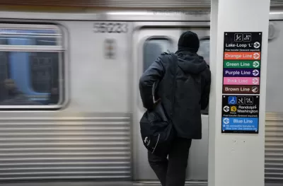 View from back of person in black clothes and hat waiting to board train at Chicago train station with blurry train in front of them.