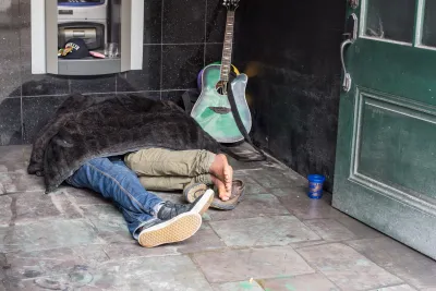 Two people sleeping under a blanket on the street in New Orleans next to a guitar