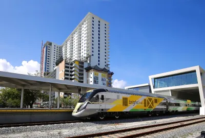 Brightline train driving out from station with tall apartment building in background.