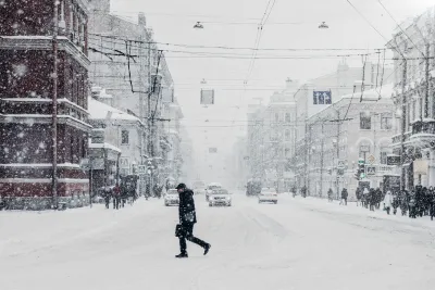 Man walking through snow in city with snow falling.