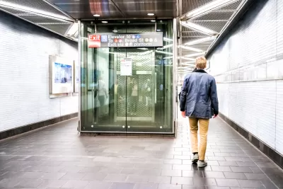 Man walking away past glass elevator in brightly lit New York City subway station corridor