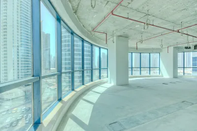 Curved window wall in vacant high-rise office building with light concrete floor and walls viewed from inside.