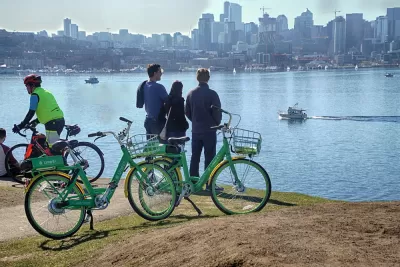 Three people standing next to Lime bikeshare bikes looking out over water toward the Seattle skyline