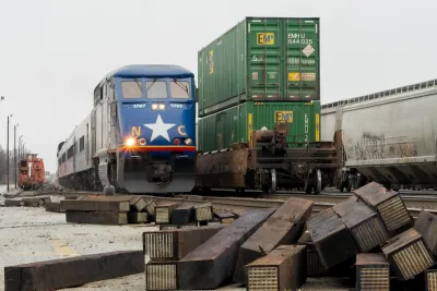 Dark blue Amtrak train passing green shipping containers on freight train in Greensboro, North Carolina.