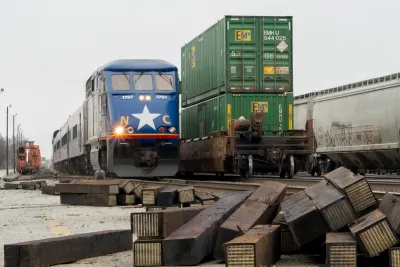 Blue Amtrak train with white star on front next to freight train with double-stacked green shipping containers.