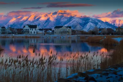 View of houses against backdrop of snowy mountains from across a lake at sunset or sunrise