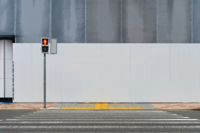 Crosswalk leading to sidewalk and blank construction wall with pedestrian crossing light