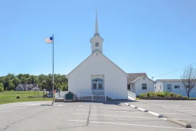Small white church with steeple with asphalt parking lot in front.