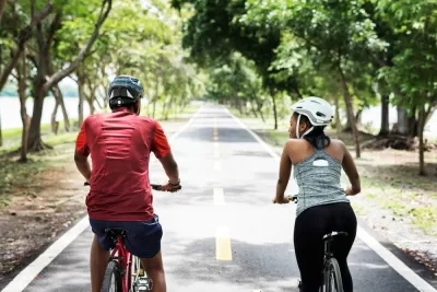 Two people riding bikes with helmets on paved park trail
