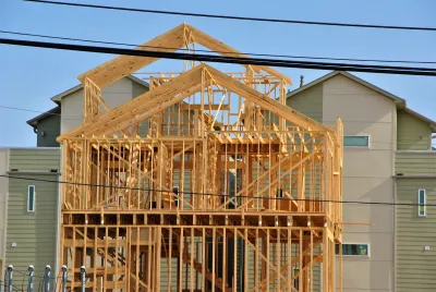 Wood-framed townhomes under construction in Houston, Texas with light green two-story building in background.