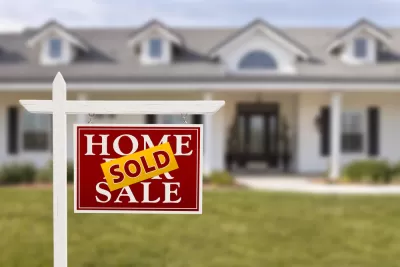 For sale sign with SOLD sign pasted over it in front of white suburban house