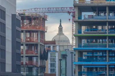 View of neoclassical dome with statue on top through construction of high-rise buildings in Washington DC.