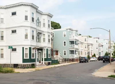 Corner of block with light-colored three-story wooden apartment buildings in Boston, Massachusetts.