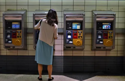 Woman in skirt and sweater using ticketing machine in NYC subway station.