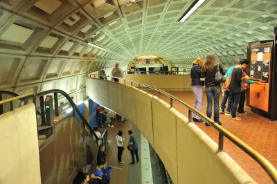View from second-story level in Washington DC subway station with riders looking at maps and taking escalator down.