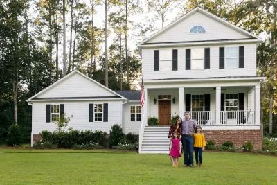 Family with woman, man, and two kids standing in front of white two-story traditional US home.