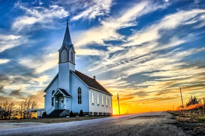 Rural white wooden church with tall steeple against sunset light in rural Kansas.