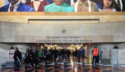 Crowd at entrance to pedestrian tunnel in Los Angeles Union Station with sign for trains and large mural above tunnel entrance. 
