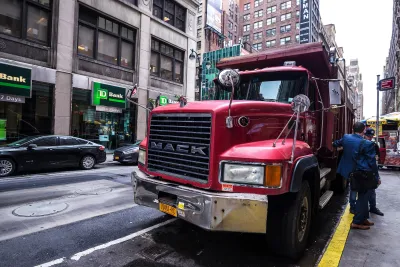 Large red freight truck parked curbside on street in New York City with two men in suits standing next to it.