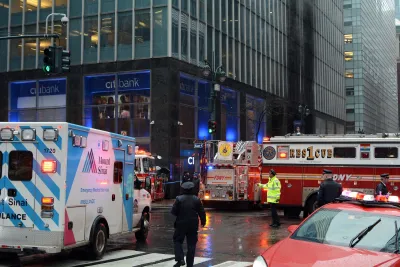 Fire truck, ambulance, and other emergency vehicles circled around a New York City intersection with police officer directing traffic in middle.