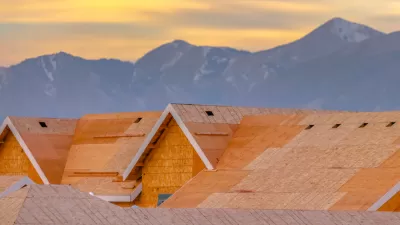 Close-up of wood-frame houses under construction with mountains in the background against sunset sky