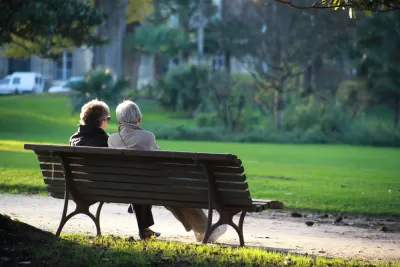 View from back of two elderly people sitting on park bench