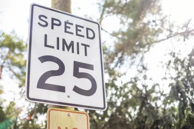 Black and white 25 mph speed limit sign on post with trees in background