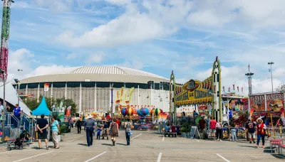 Crowded carnival or fair with rides in parking lot of Houston Astrodome, historic domed stadium.