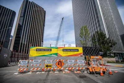 Street closure signs in front of construction wall and banner touting LA Metro's subway extension in front of high-rise buildings.