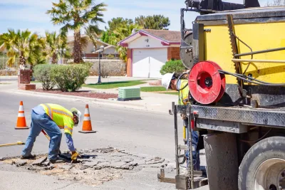 Worker in jeans and yellow safety vest repairing pothole on street in El Paso, Texas.