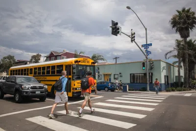 Two people with backpacks on crossing a crosswalk in front of a yellow school bus in San Diego, California.
