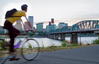 Cyclist on bike path in Portland, Oregon with bridge over river and city skyline in background.
