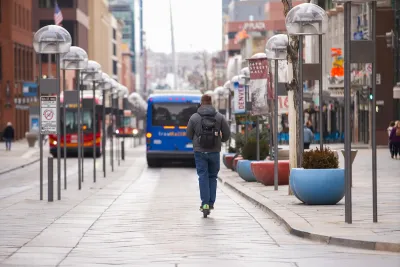 Man rides green share scooter on protected bus lane with blue bus in front of him in Denver, Colorado.