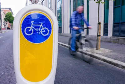 Close-up on plastic bollard with blue and white bike logo in bike lake in Ireland with blurred bike rider in background.
