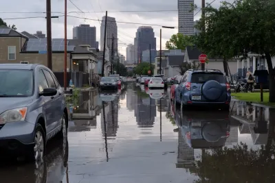 Carsparked on flooded street in New Orleans with downtown high-rises visible in background.