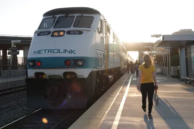 A woman in a yellow top walks down a train platform next to white Metrolink train in Anaheim, California.