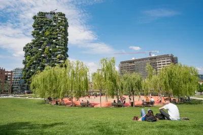People sitting on grass in park in Milan, Italy with grove of willows and a vertical forest skyscraper in background.