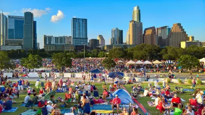 Crowd of people sitting on lawn on July 4 in Austin, Texas with downtown skyline visible in background.