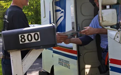 Close-up on postal worker hanging mail out of a mail truck to resident standing in front of black mailbox.