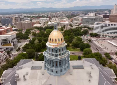Aerial view of gold Colorado state capitol building with green park and city beyond 