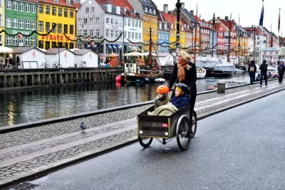 Woman riding cargo bike with two small children on Copenhagen street next to a canal