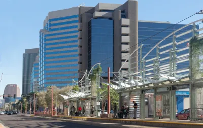 People waiting at a Phoenix light rail station under decorative shade elements.