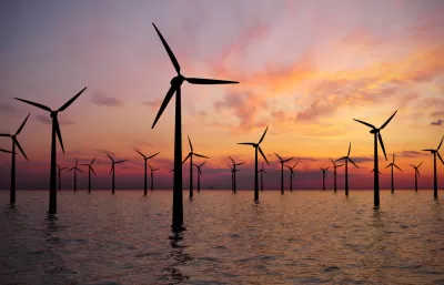 Offshore wind turbines in water against a sunset sky