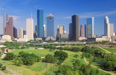 Aerial view of green Memorial Park lawns and trees with downtown Houston skyline in background