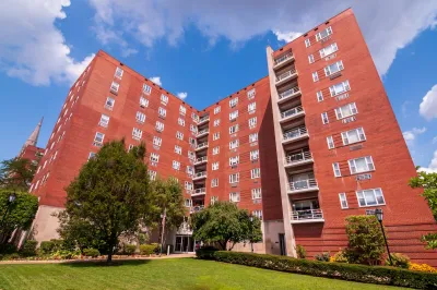 Multistory red apartment building in Pittsburgh, PA against blue sky with white clouds.