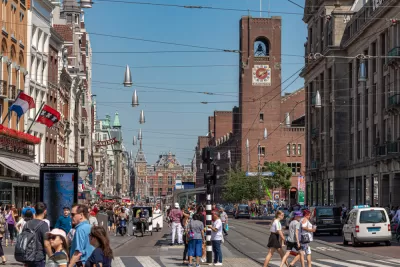 Crowded Amsterdam street with pedestrians, cars, and church in background