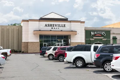 The main front entrance to the Asheville Mall, showing parking lot and cars.